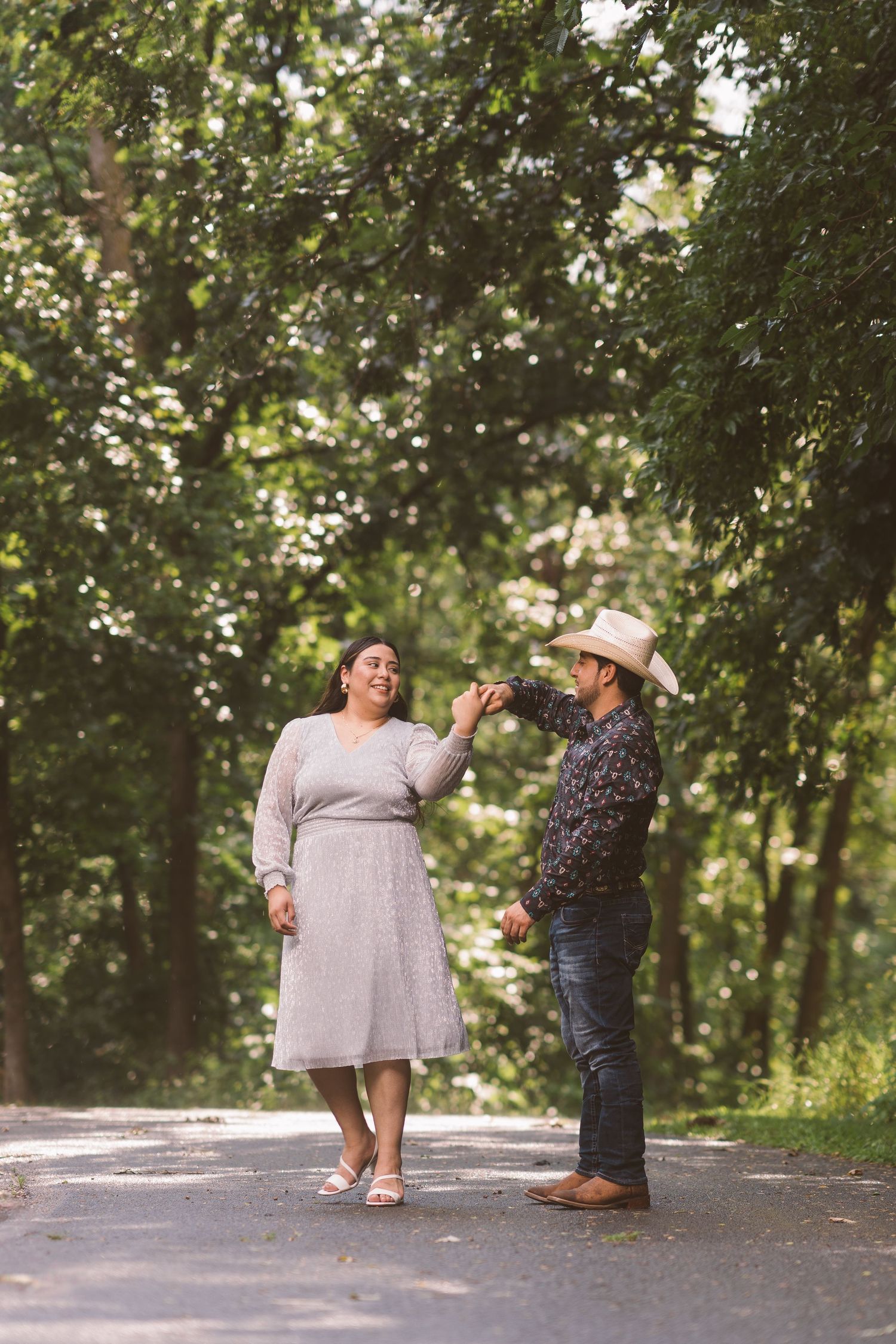 A couple shares a joyful dance moment on a tree-lined path.