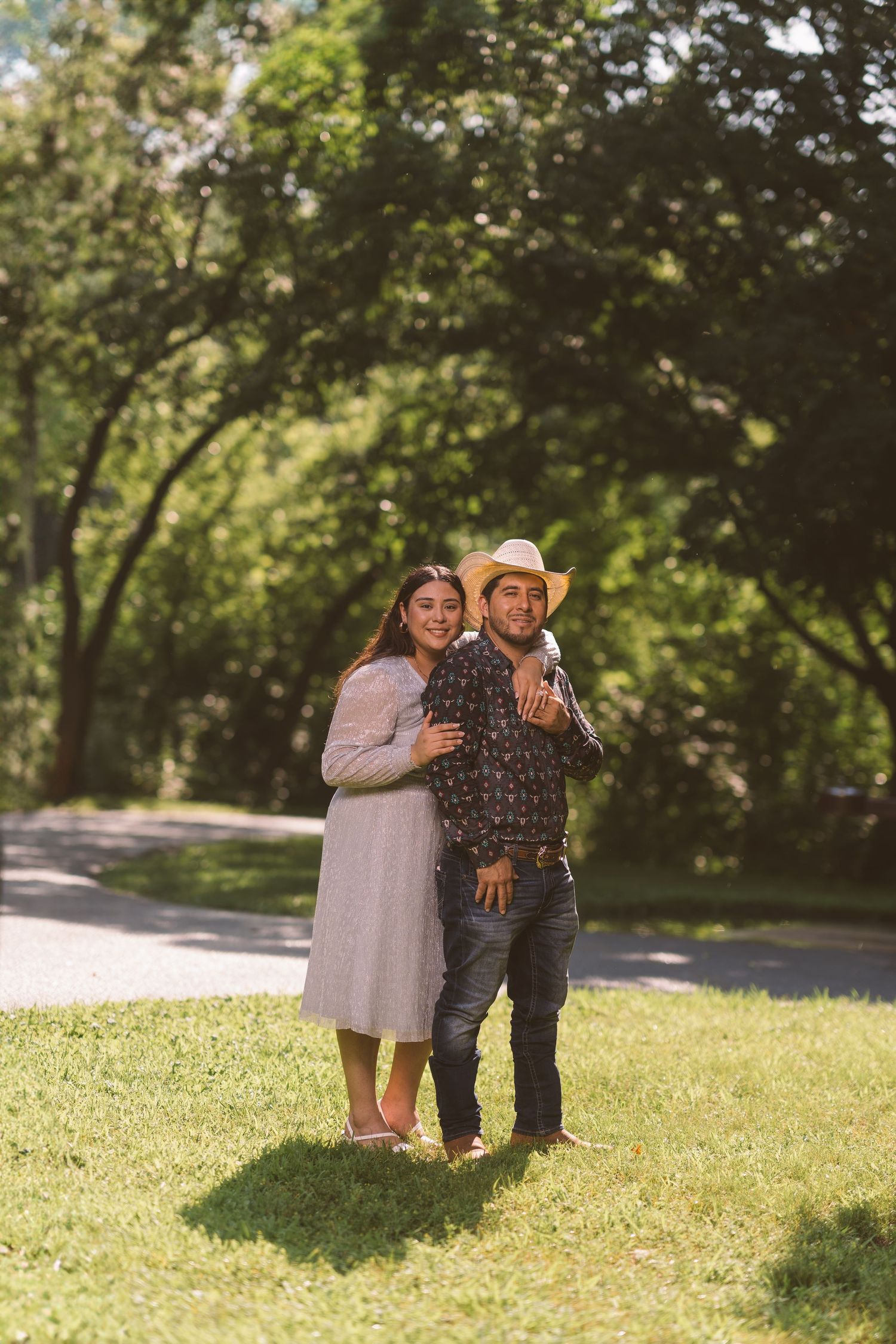 A couple poses playfully together on sunny green grass.