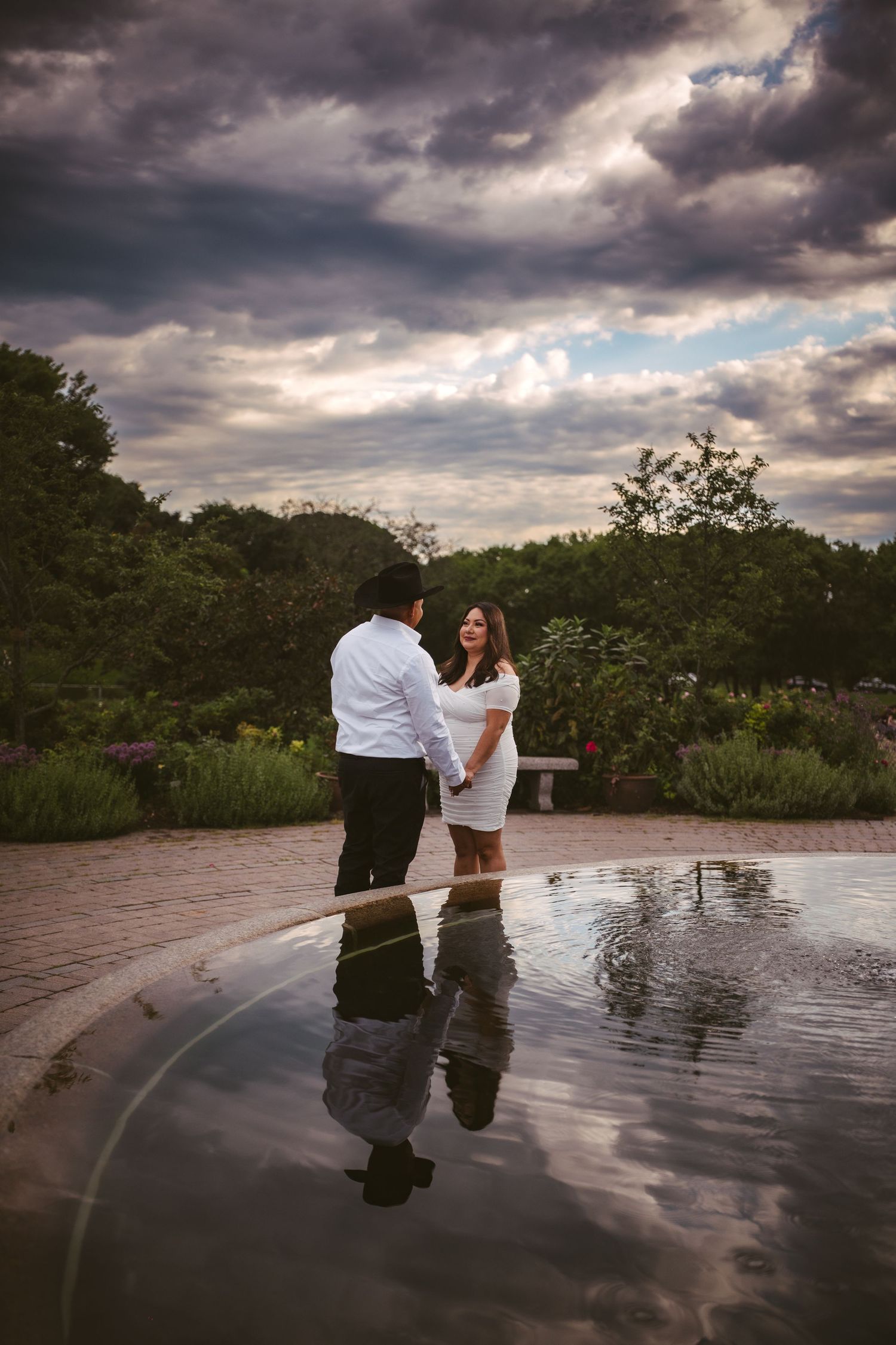 Engagement photos captured with dramatic reflections in fountain water under stormy skies.