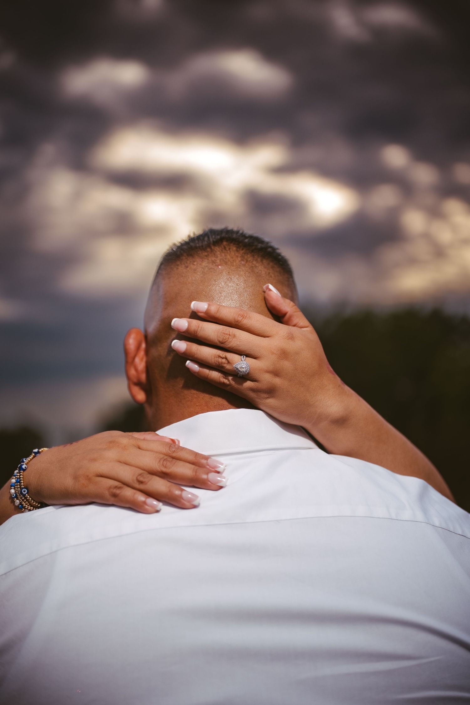Close-up detail of hands tenderly embracing against dramatic cloudy sky.