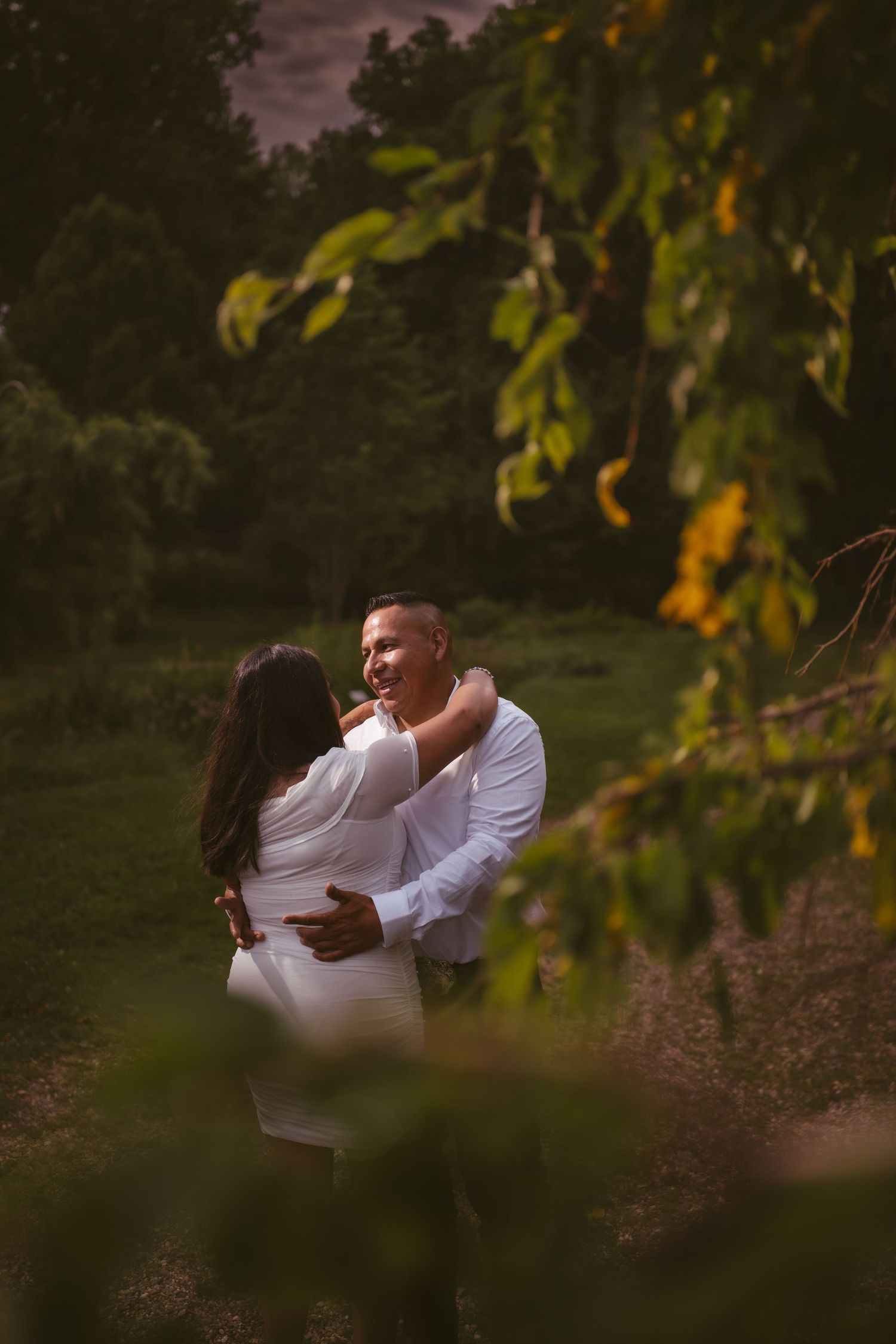 A couple shares a tender moment among autumn leaves in a romantic outdoor setting.