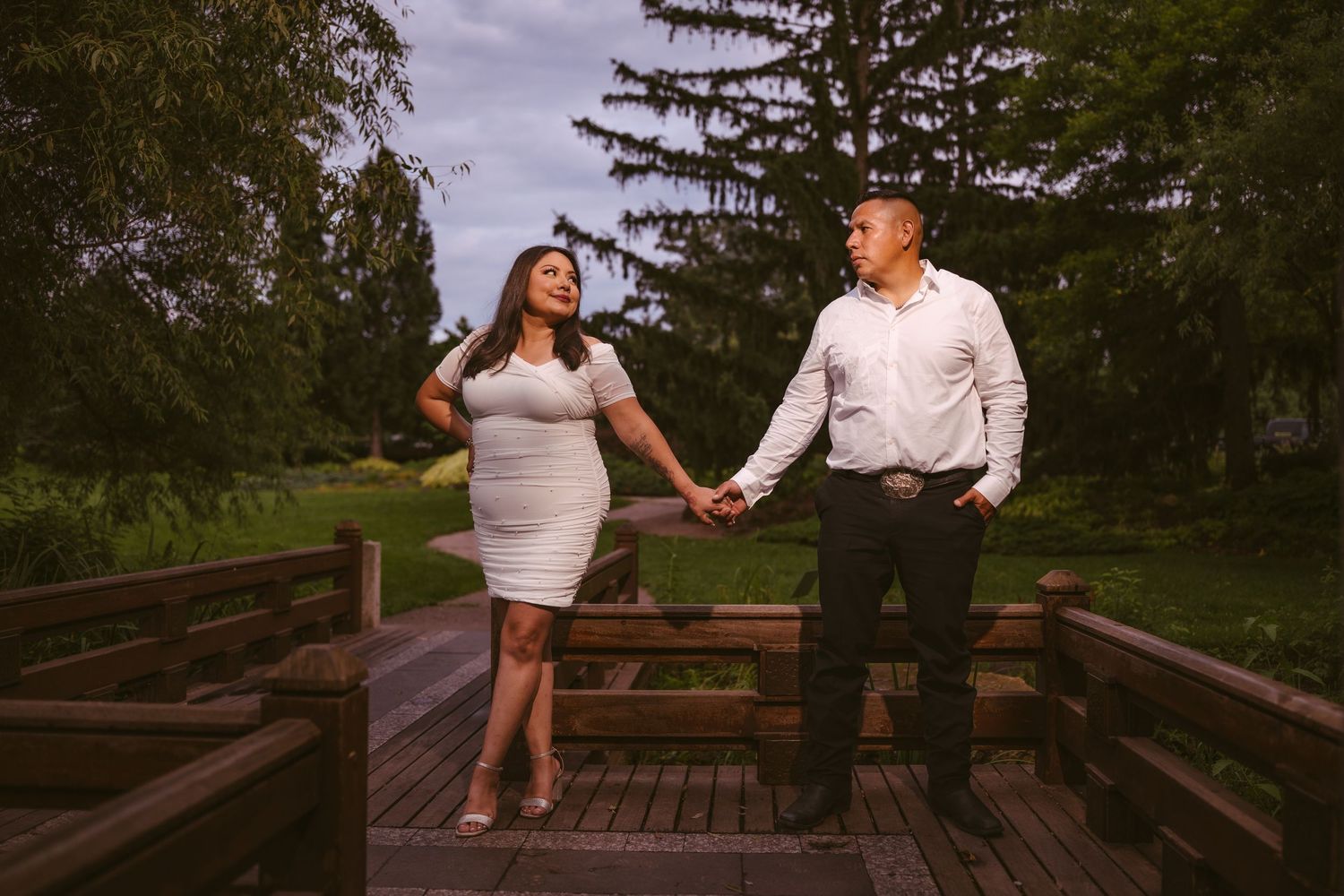 Two people sit together on a wooden deck surrounded by pine trees in a park setting.