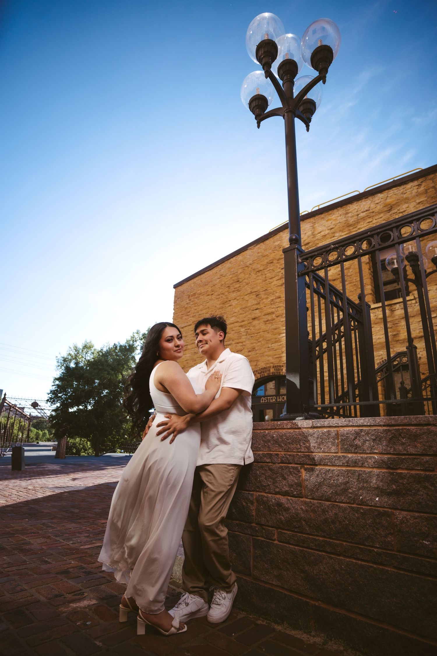 Couple embraces romantically beneath ornate street lamp outside historic brick building at sunset.