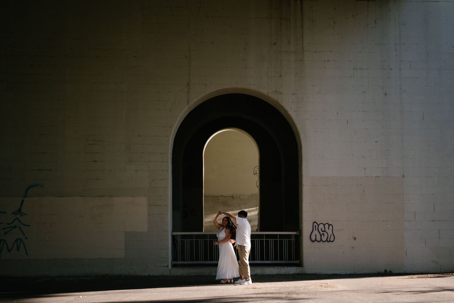 Couple embracing under an arched tunnel with graffiti, bathed in dramatic light and shadow.