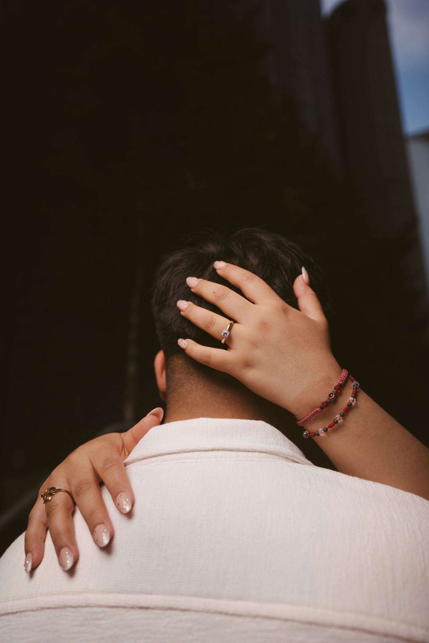 Close-up of a woman's hand with engagement ring and bracelet resting on a man's head and shoulder.