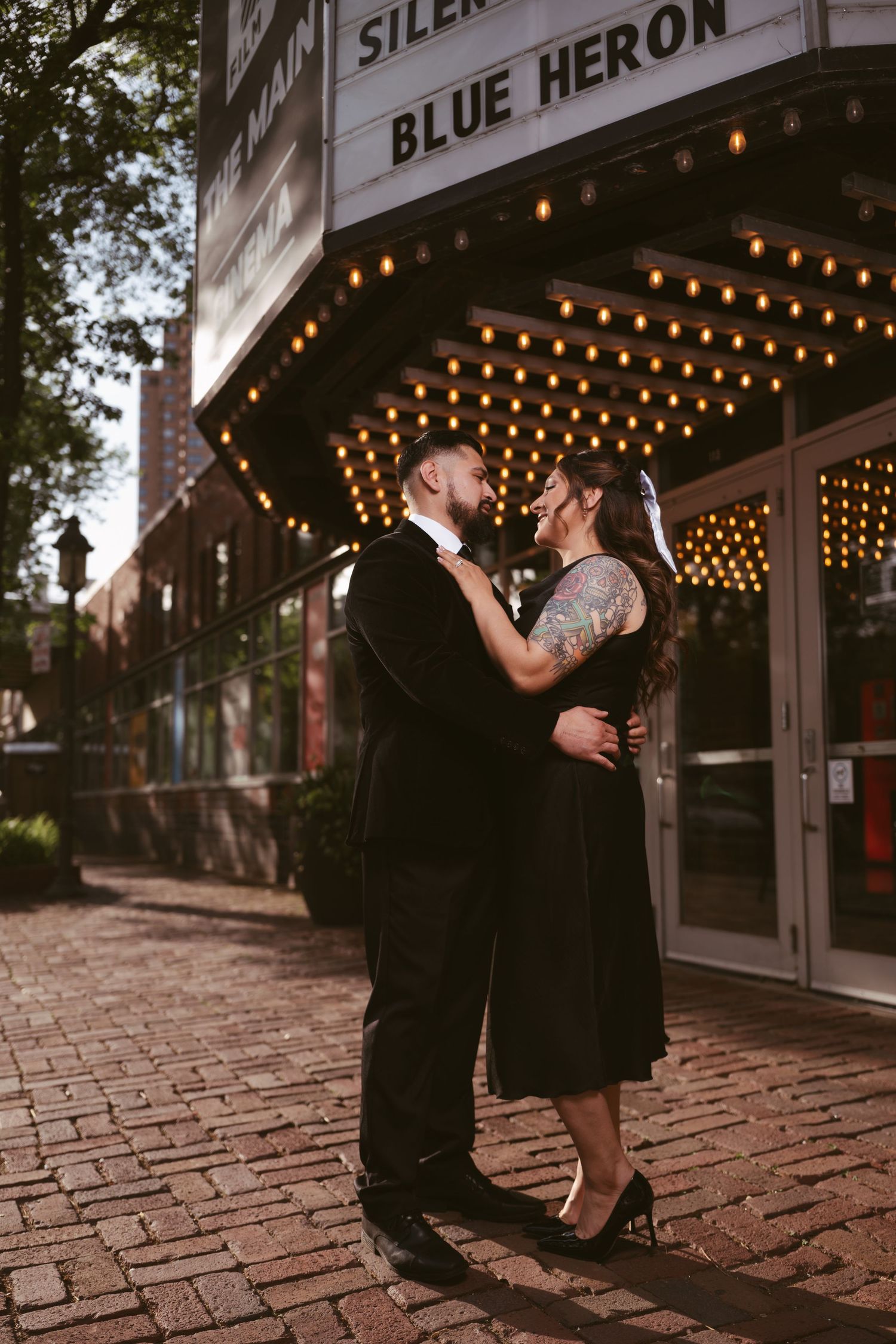 Couple in black attire sharing a romantic moment under the glowing Blue Heron theater marquee lights.