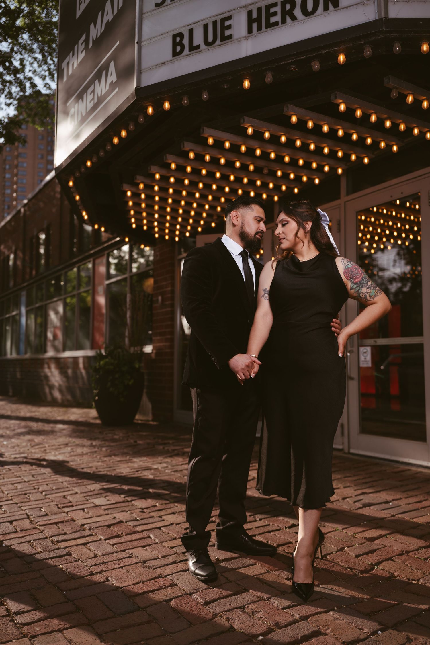 Couple in black attire holding hands outside Blue Heron Cinema marquee lights at night.