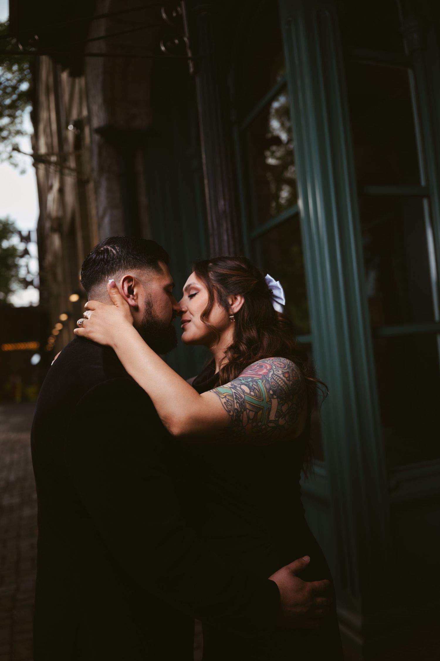 Tattooed couple sharing an intimate embrace near a vintage building at dusk.