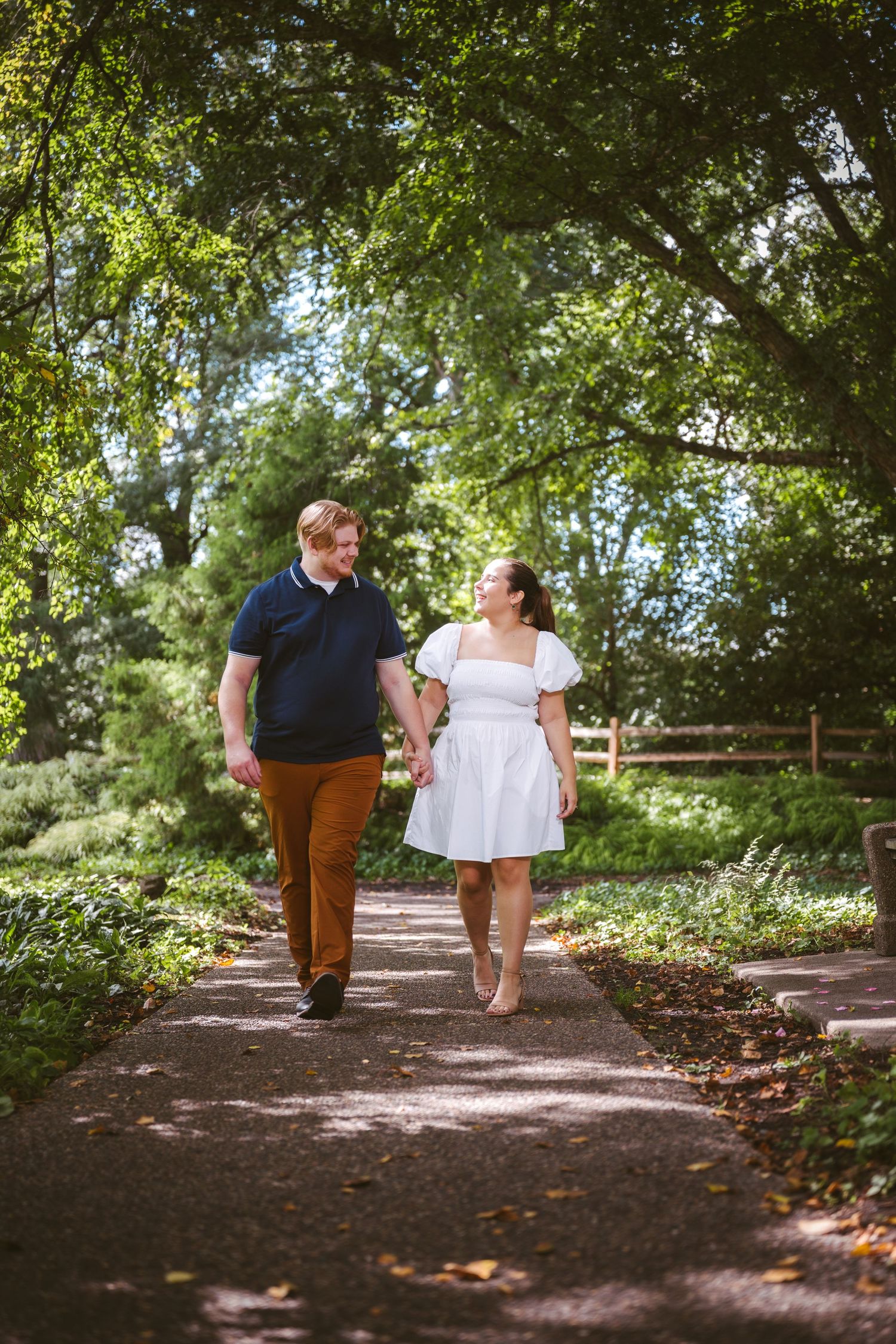 A couple walking together on a tree-lined path in a garden setting.