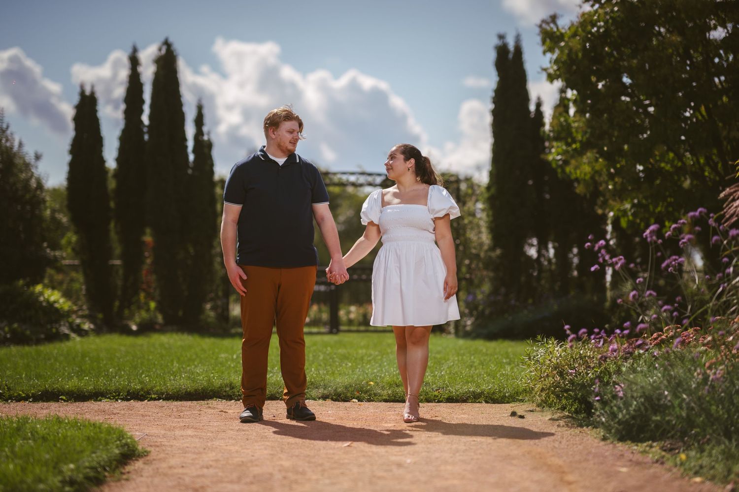 A romantic engagement photo series in a garden with cypress trees and pathways.