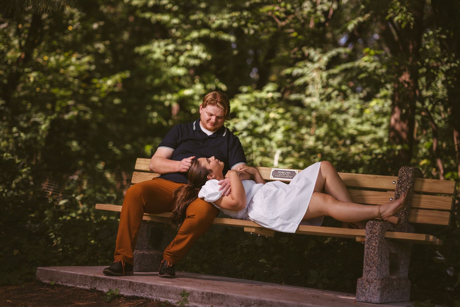 A couple shares intimate moments on a wooden bench in a lush garden setting.