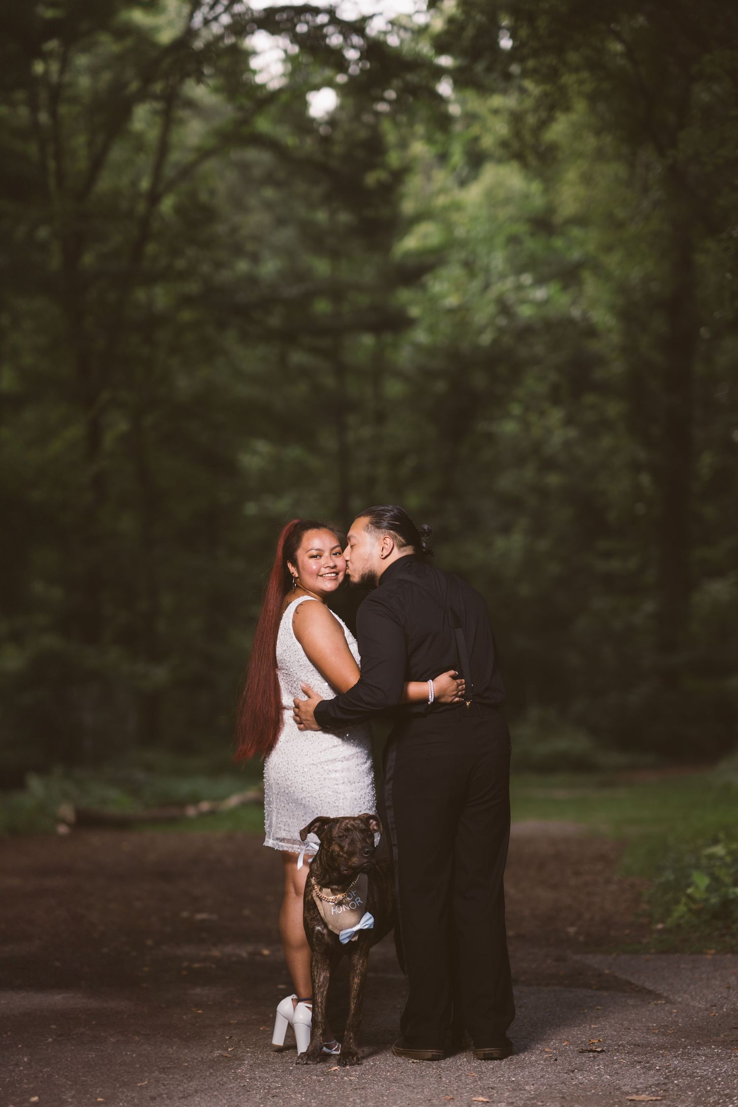 A romantic couple shares an intimate moment on a wooded path at dusk.