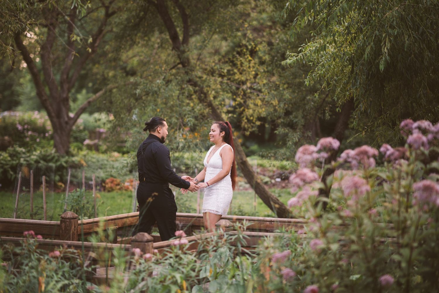 A couple walks hand in hand through a garden path with pink flowers blooming.