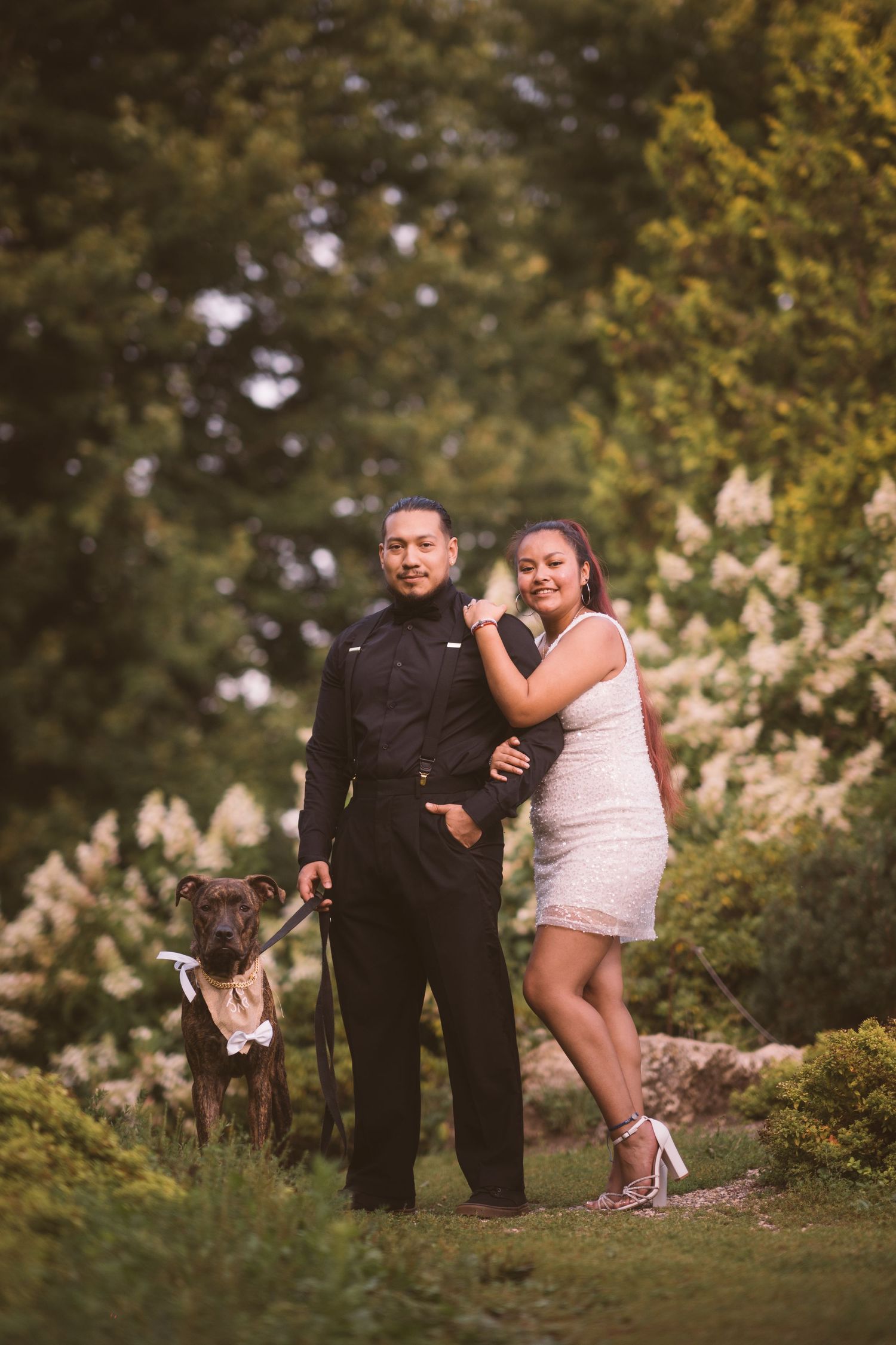 A playful couple poses together among blooming flowers in a garden setting.