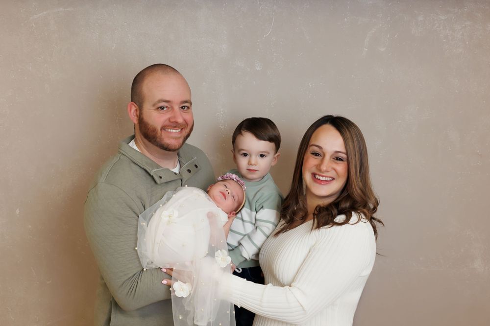 A family wearing cozy white and gray sweaters poses together against a neutral backdrop for a portrait session.