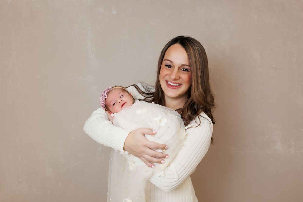 A newborn baby wrapped in white is held lovingly against a neutral beige background.