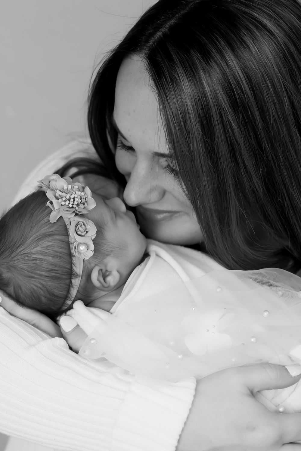 A tender black and white portrait of an affectionate moment between a baby wearing a headband and parent in soft light.