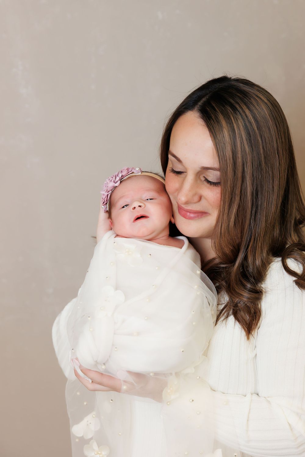 Intimate portrait of parent and newborn baby in white against neutral background.