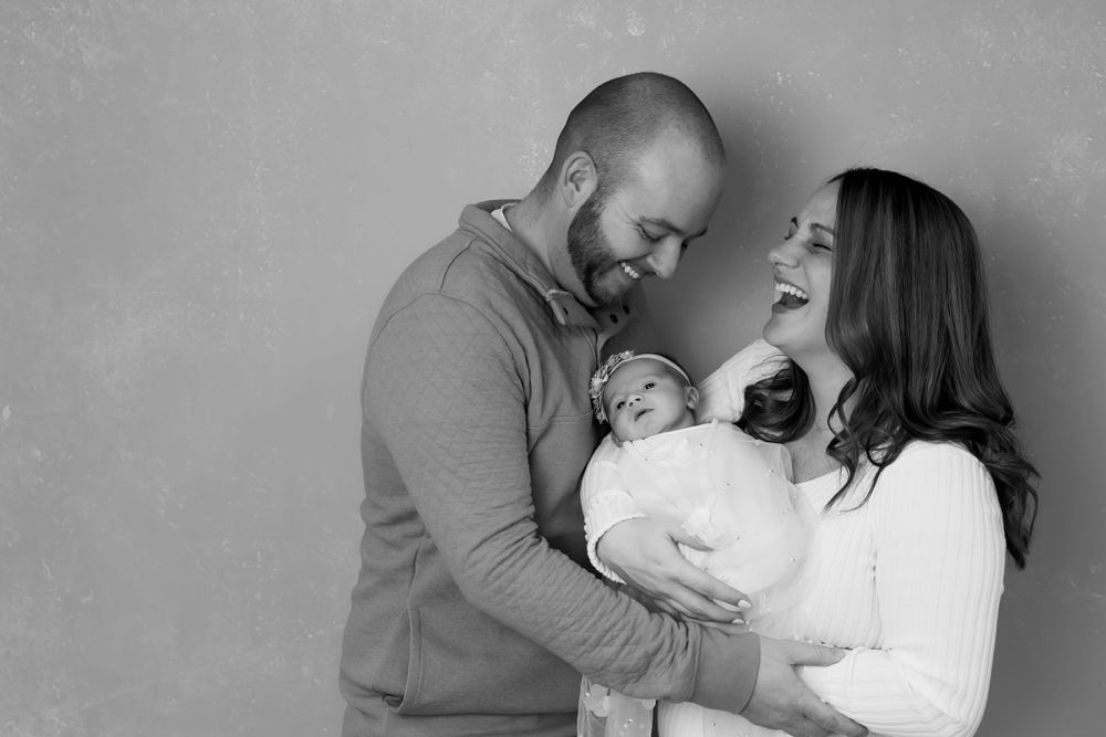 A black and white portrait of parents sharing an intimate moment while holding their newborn baby.