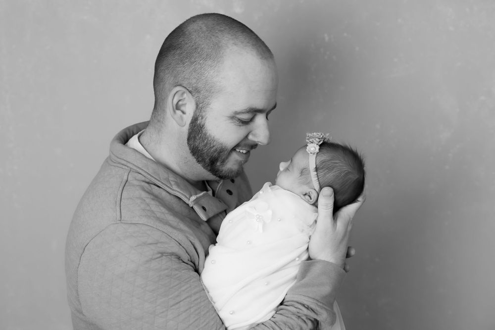 A tender black and white portrait showing a father holding and smiling at his newborn baby.
