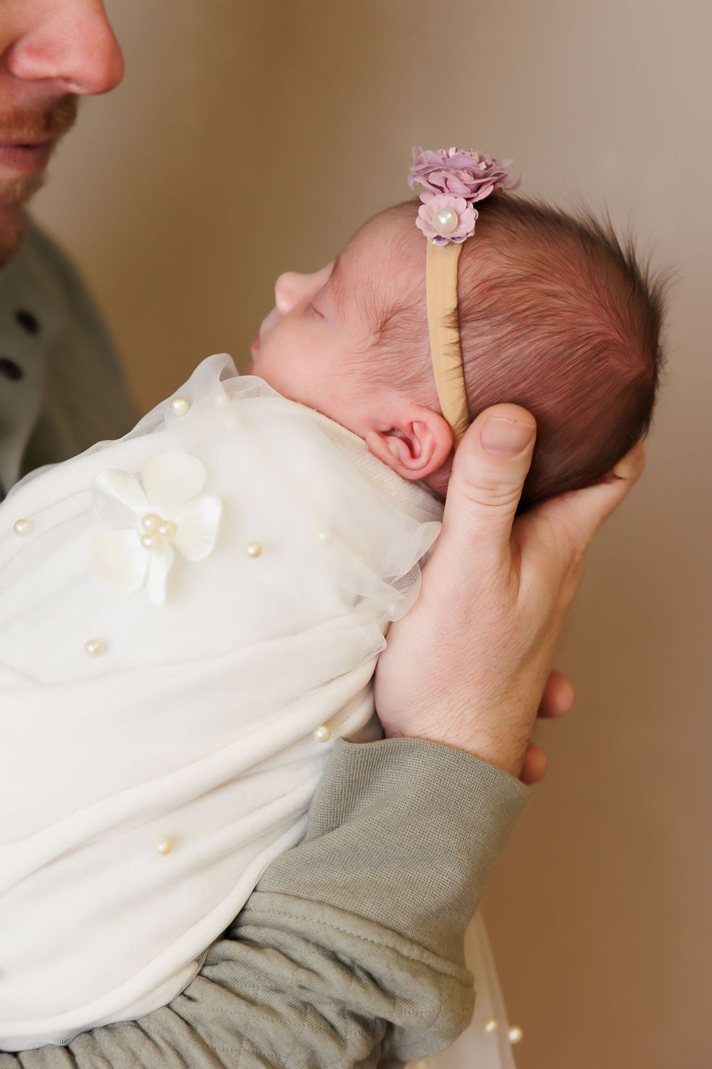 A sleeping newborn wearing a white outfit with a delicate pink floral headband.