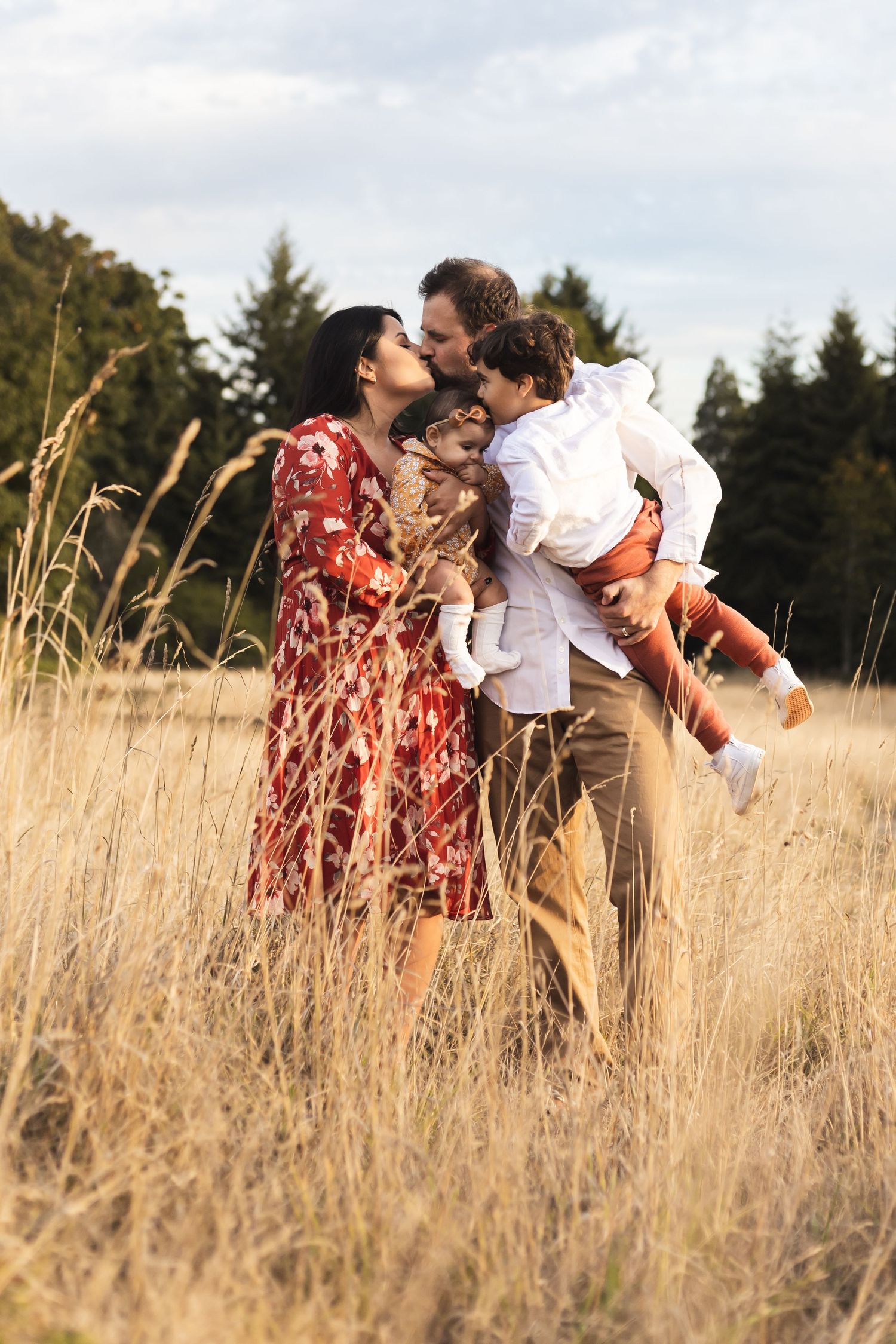 Family sharing tender moment together in tall grass field during golden hour.