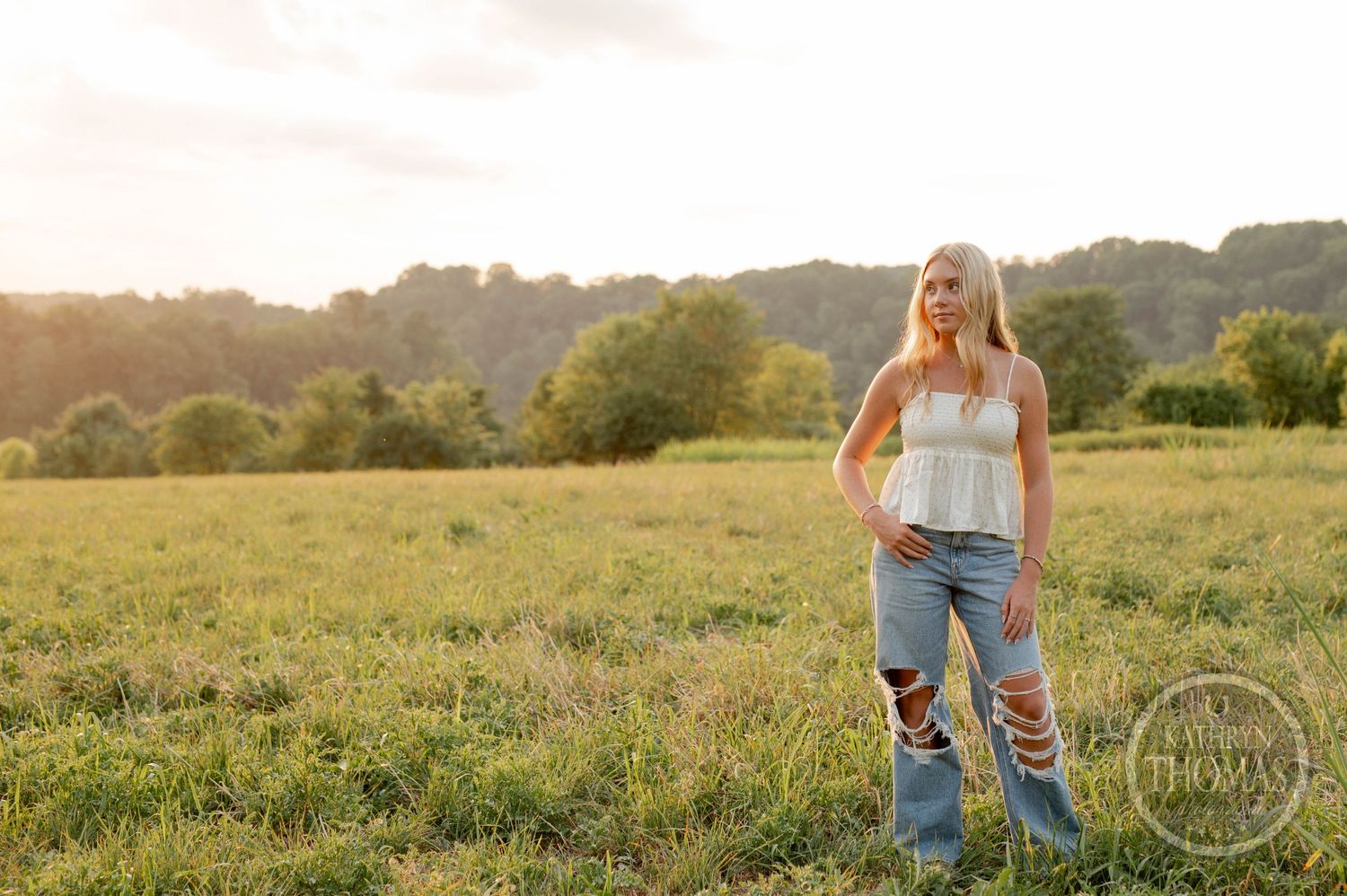 Summer fashion photography in sunlit meadow with distant treeline.