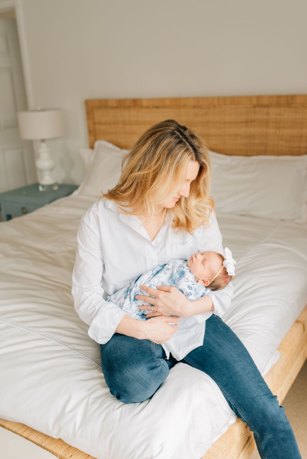 A new mother holds her baby girl while sitting on the edge of the bed while Lauren Marie photography captures the beautiful moment.