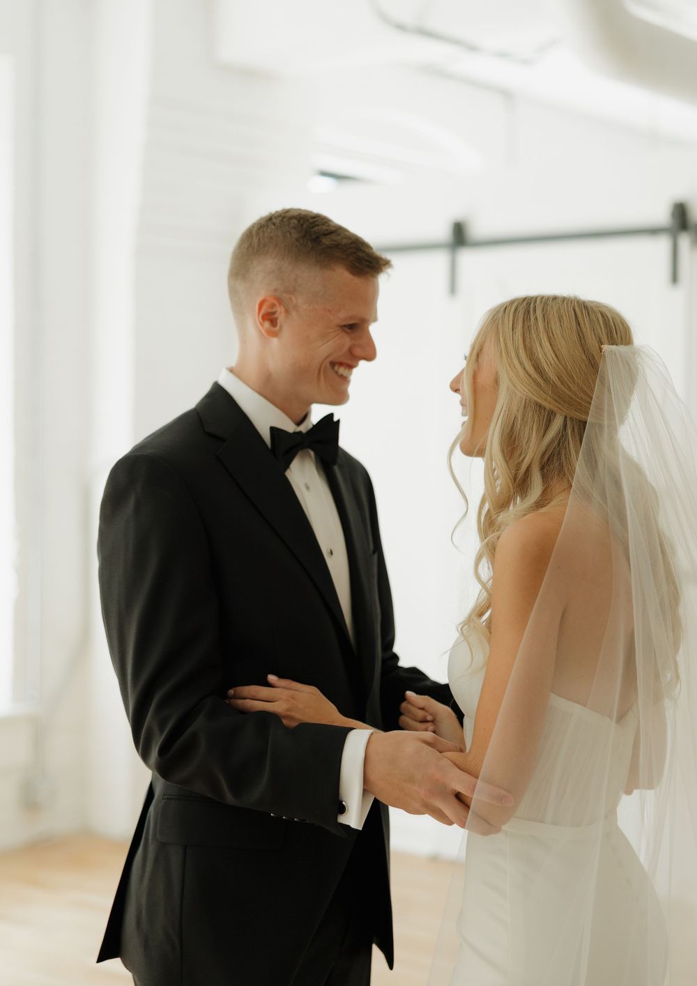 A bride and groom share an intimate first look moment in a bright white room during their wedding day.
