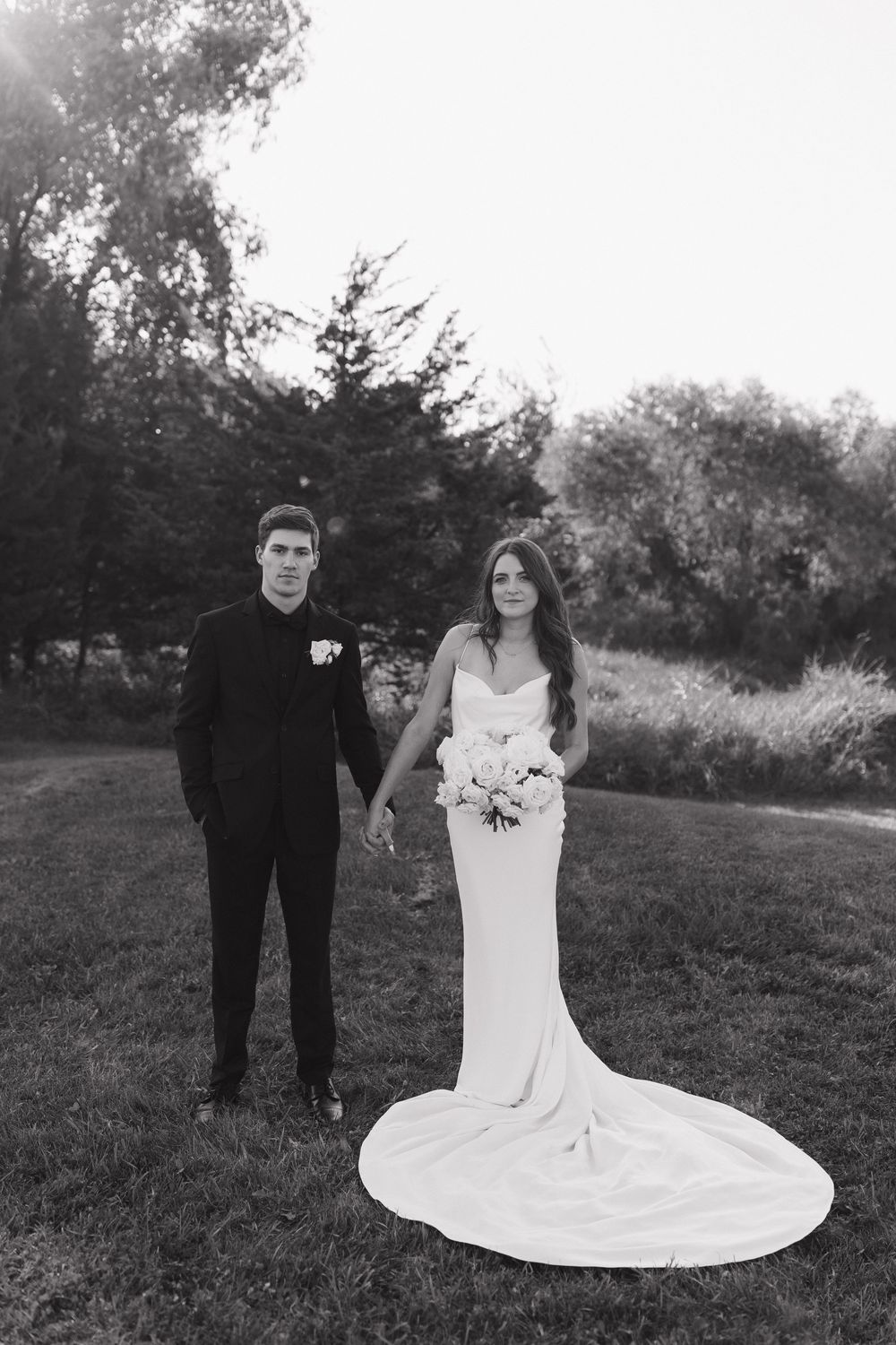 Black and white wedding portraits of a couple in formal attire posing together on a grassy hillside.