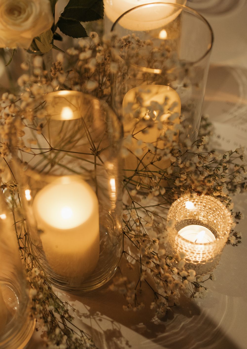 Glowing candles in glass holders surrounded by delicate baby's breath flowers create an intimate table setting.