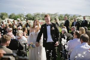 Newlyweds celebrate with guests during an outdoor wedding ceremony as bubbles float through the sunny afternoon air.