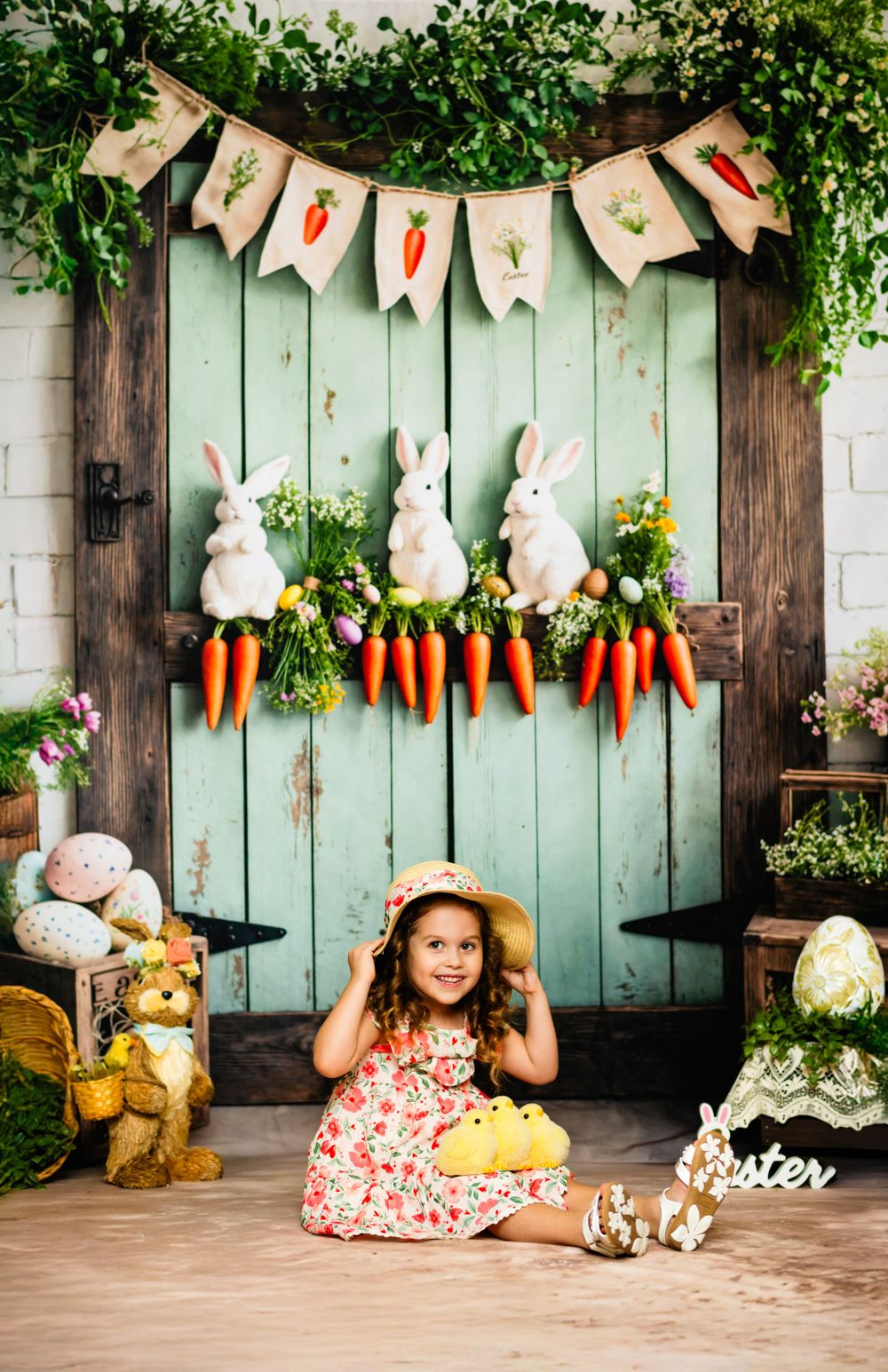 Decorative Easter scene with wooden door, hanging carrot banner, white bunny decorations and spring floral arrangements.