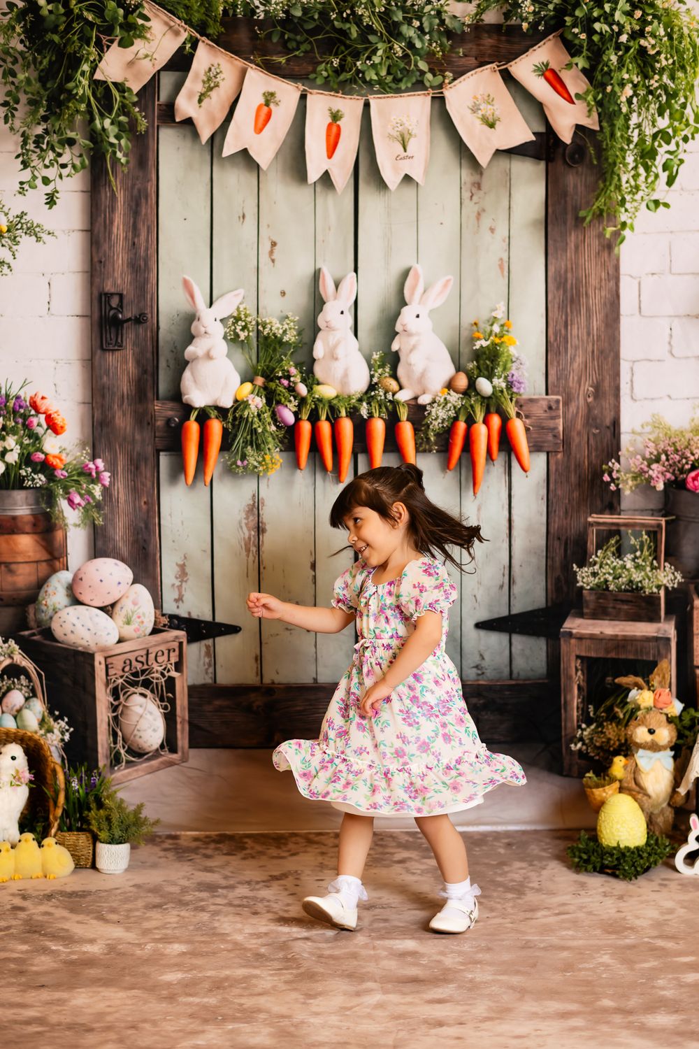 Spring Easter photo setup with white bunnies, carrots, and decorative banner against rustic wooden door backdrop.