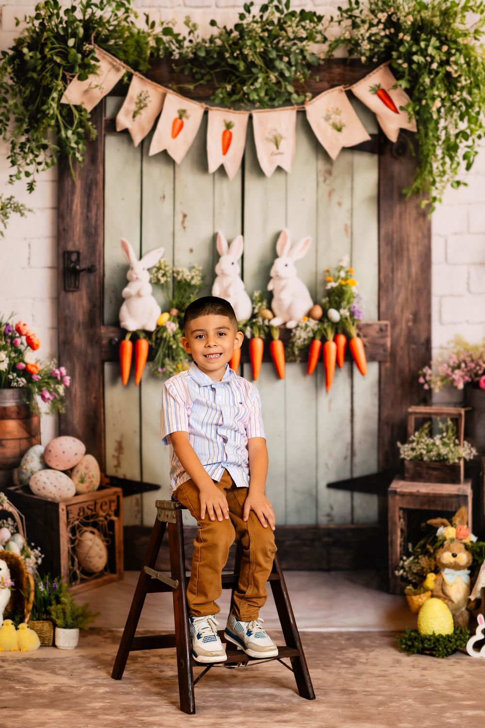 Easter photo backdrop with decorative bunnies, carrots, banner and rustic wooden door behind a small stool.