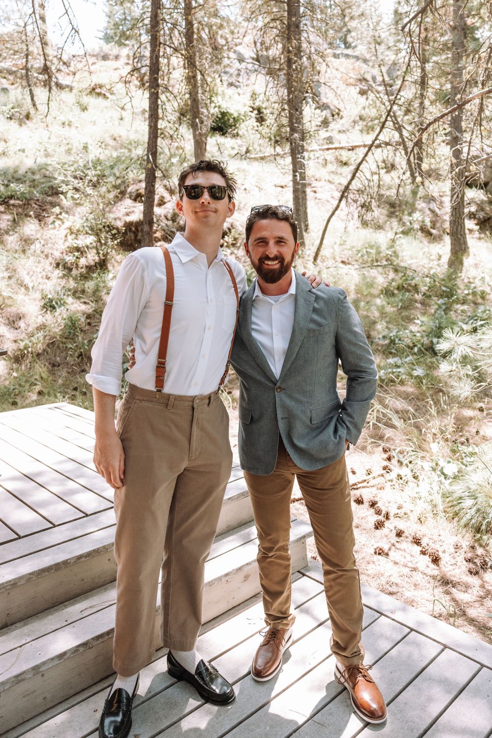 Two formally dressed guests stand on wooden deck steps in forest setting.