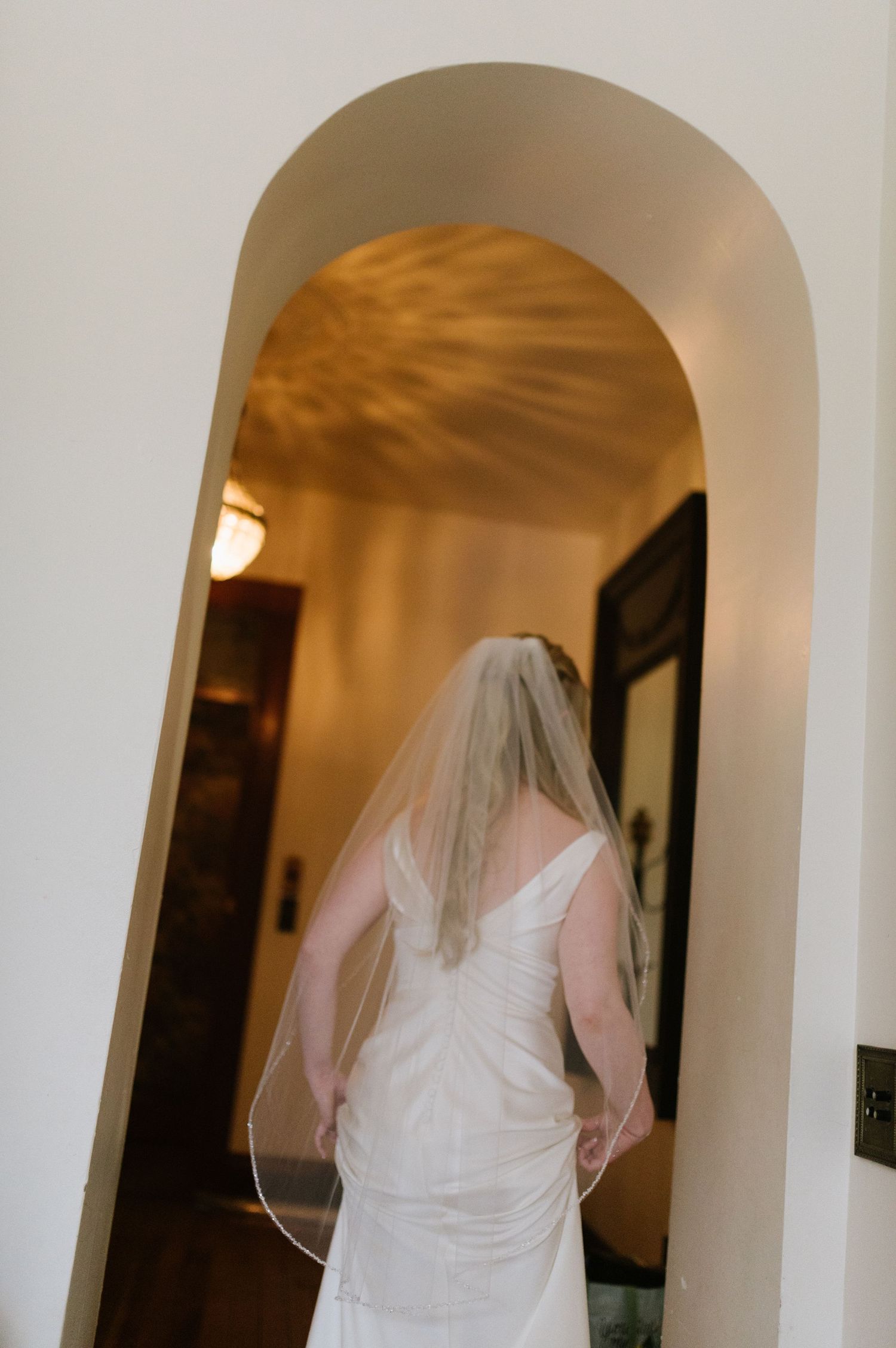 A wedding dress silhouette framed in an arched doorway with warm lighting.