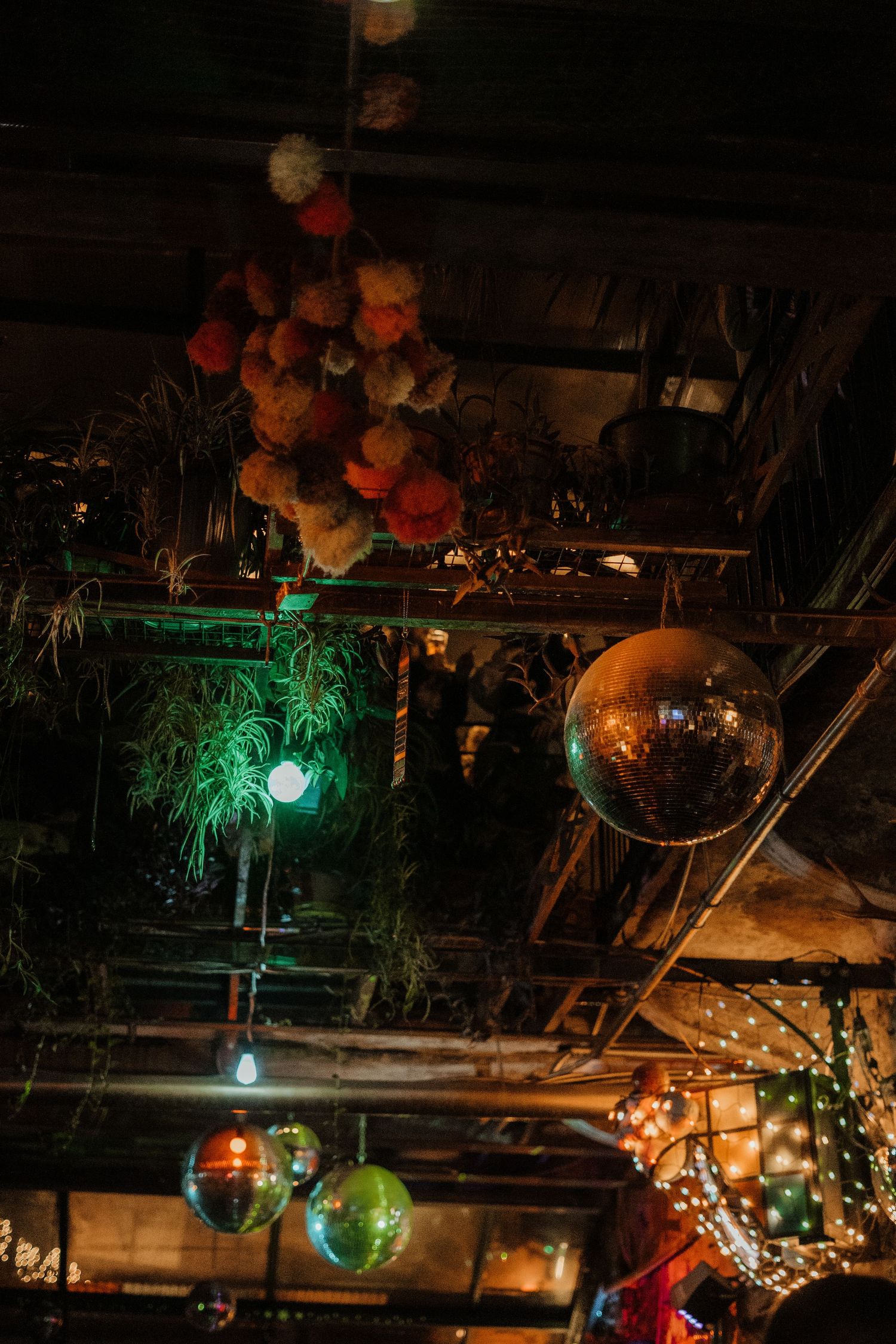 Round disco balls and paper lanterns hanging from industrial ceiling with green ambient lighting and string lights.