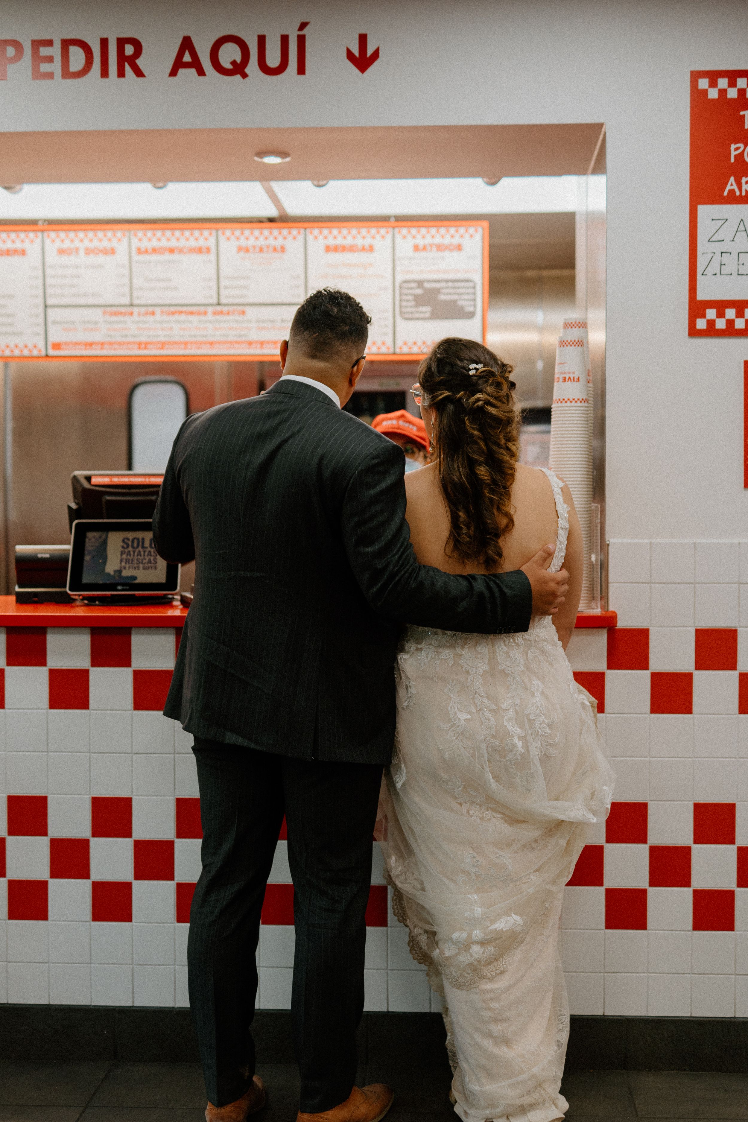 A couple in wedding attire placing their order at a retro-style diner counter with red and white checkered tiles.