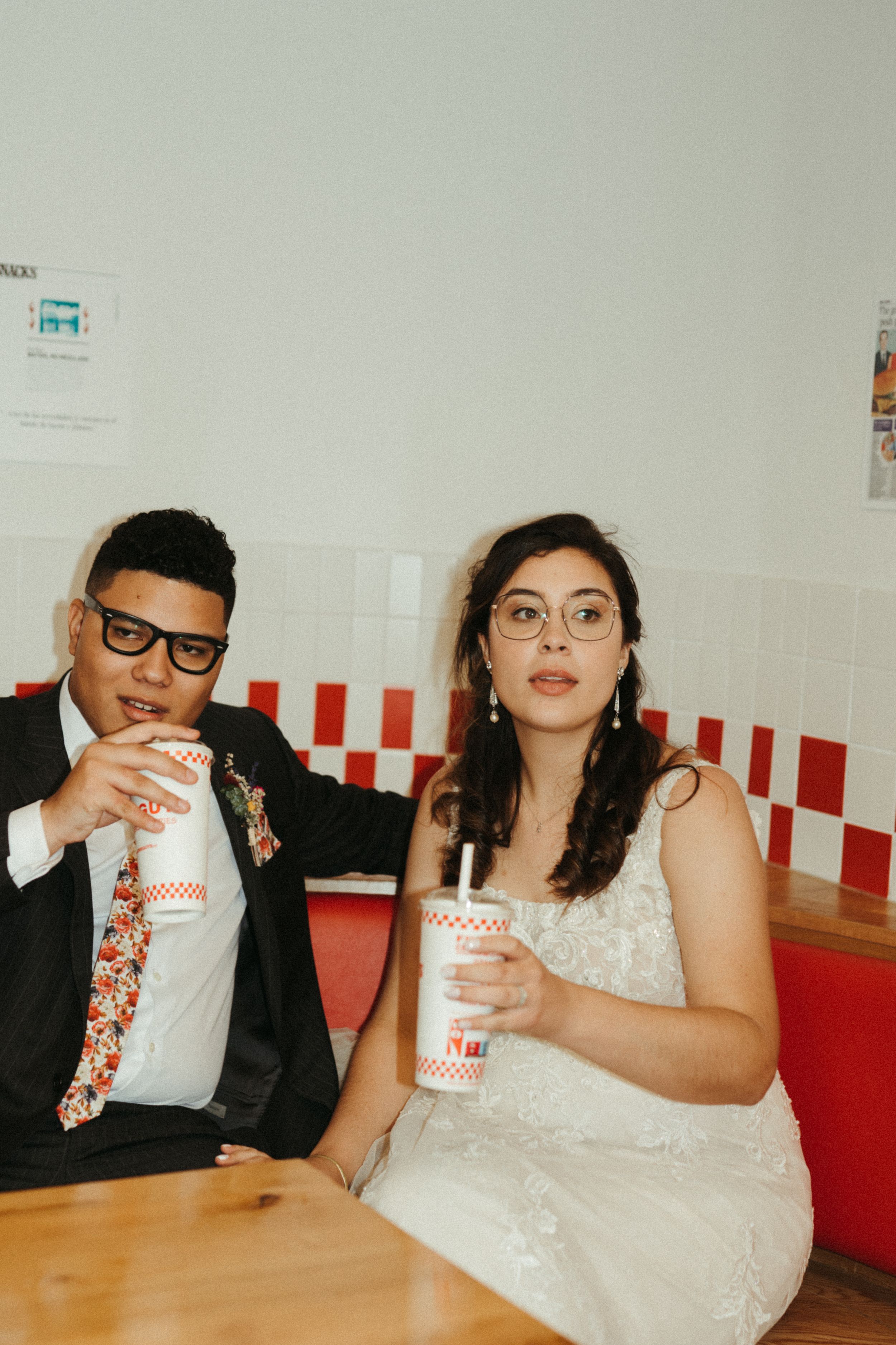 A couple in wedding attire enjoying drinks at a retro-style diner with red and white decor.