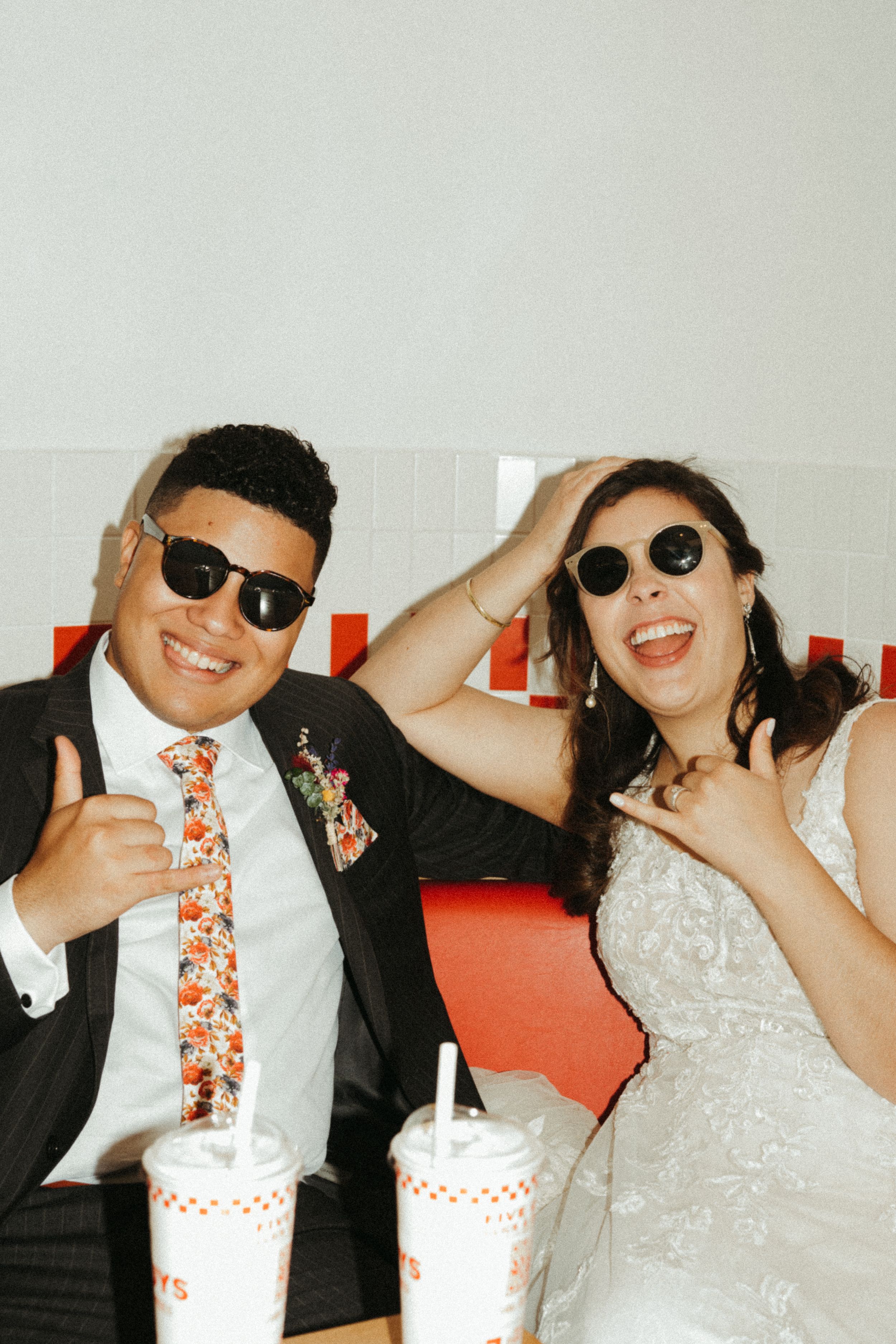 A fun wedding moment with a couple in sunglasses posing playfully with Whataburger drinks at their reception.