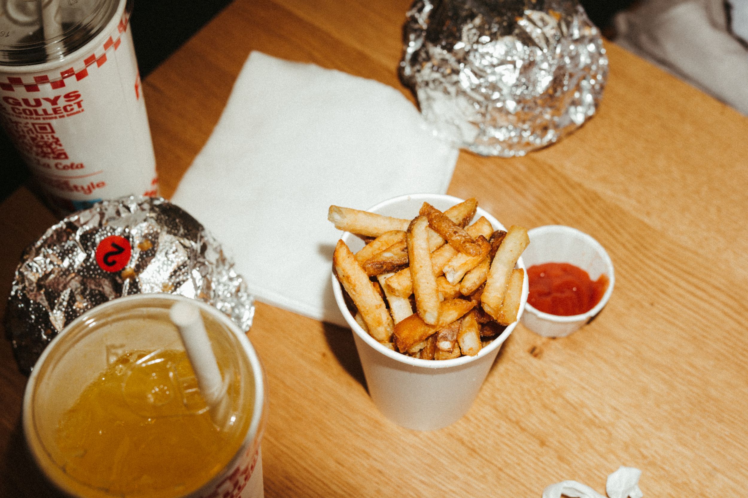 Golden french fries served in a paper cup with ketchup dipping sauce alongside a glass of beer on wooden table.