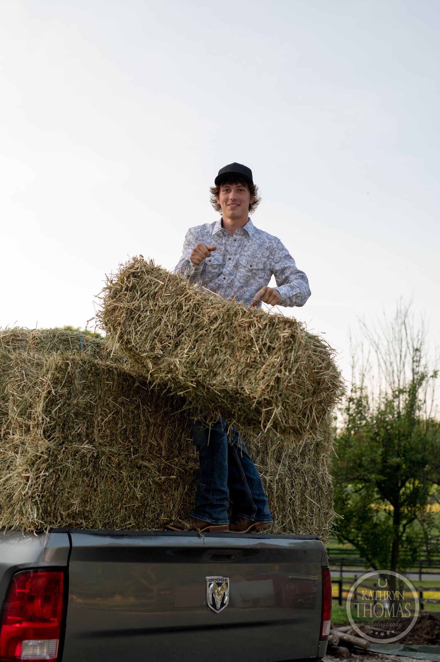 Someone stands on hay bales in the back of a pickup truck at dusk.