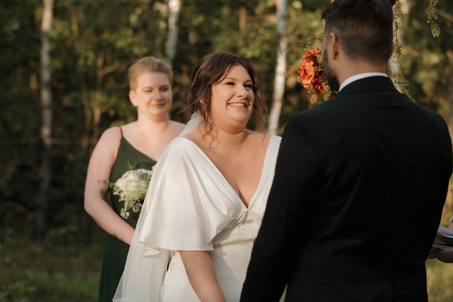 Joyful outdoor wedding ceremony with bride in flowing white dress and groom in black suit during golden hour.