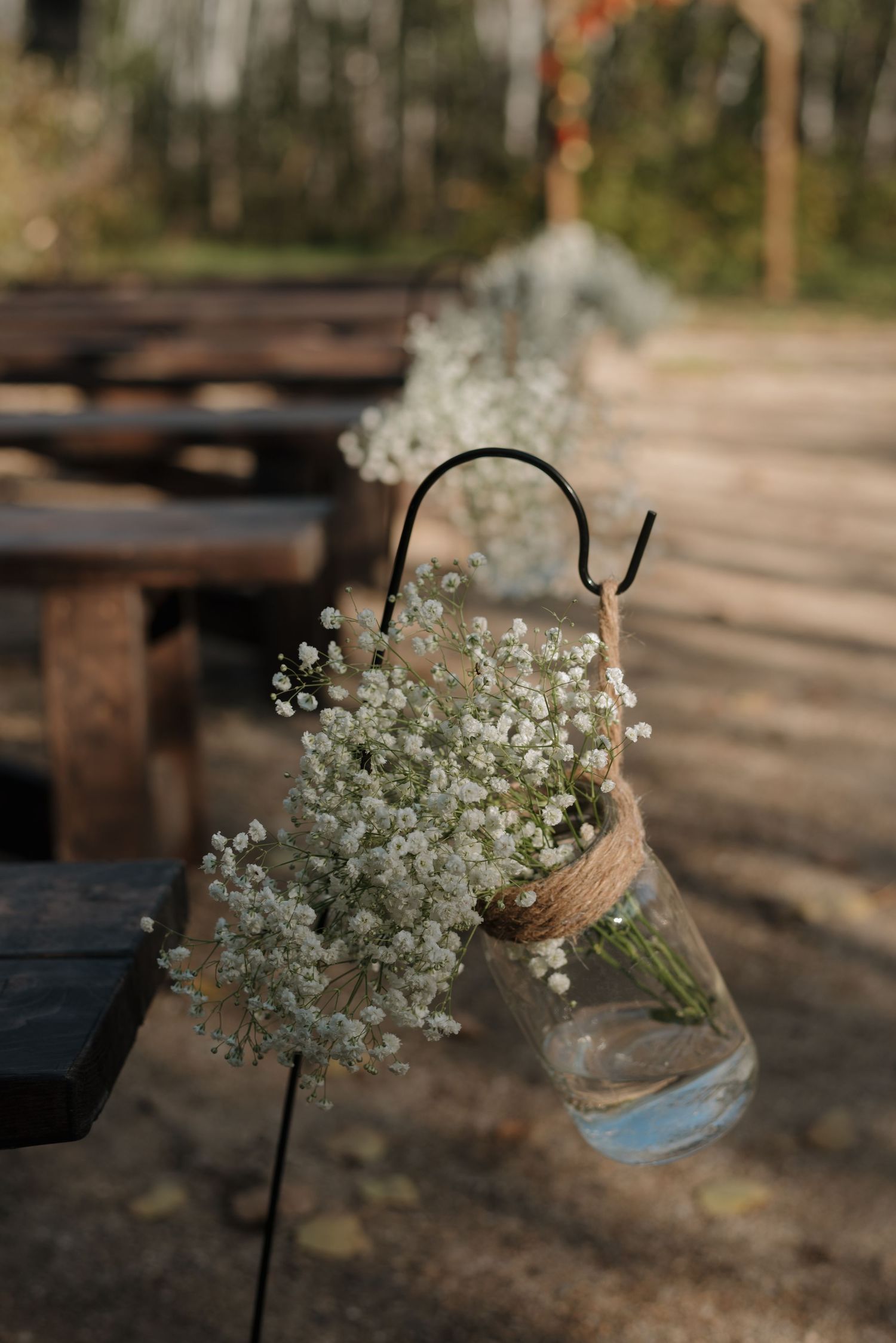 Baby's breath flowers arranged in a hanging mason jar vase against a rustic wooden background in soft natural lighting.