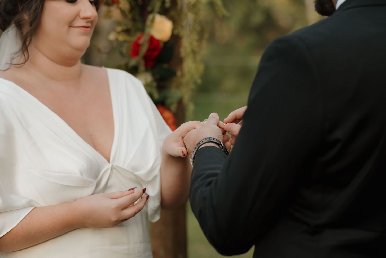Close-up shot of hands exchanging rings during an outdoor wedding ceremony with greenery in background.