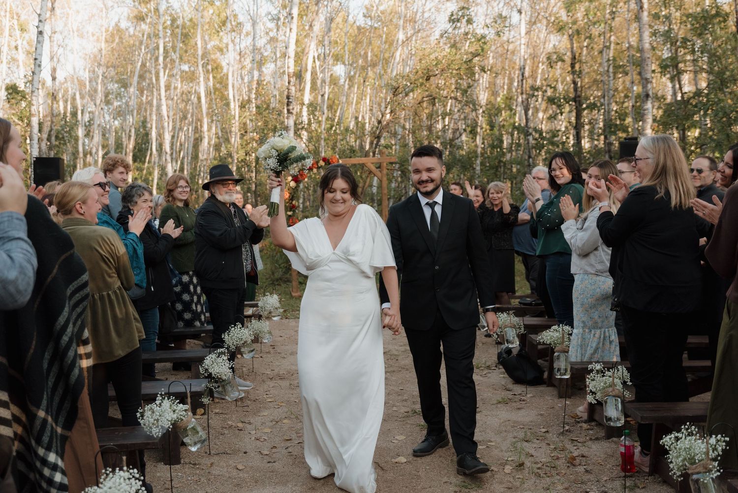A joyful outdoor wedding ceremony surrounded by aspen trees during a fall day in a natural forest setting.