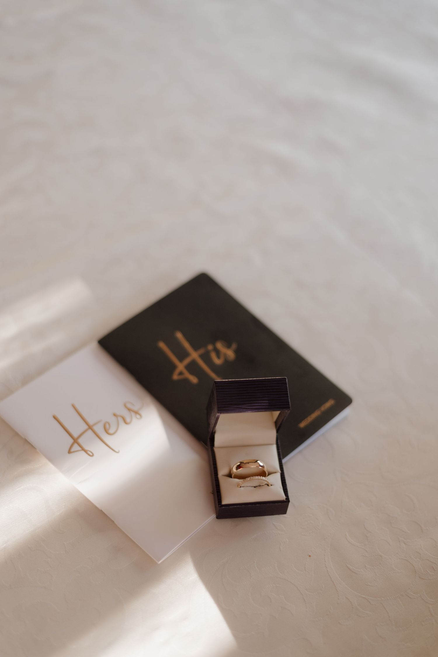 Elegant ring box with gold 'Hers' text on white and black boxes casting soft shadows in natural light.