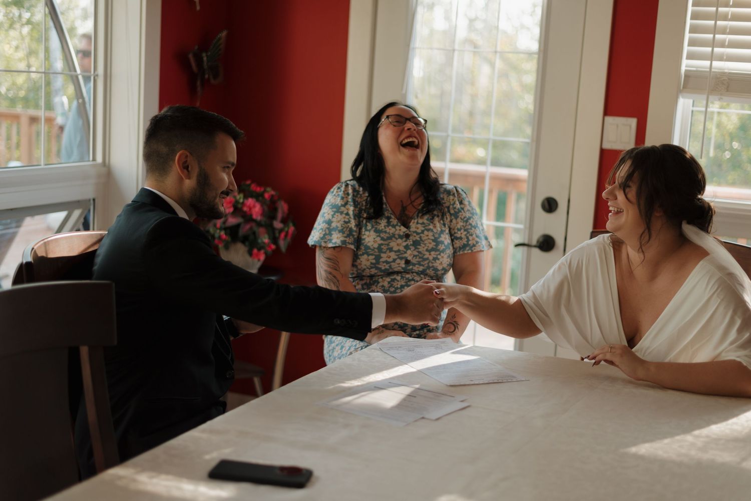 Three people sitting at a dining table share a joyful moment while looking at paperwork together.
