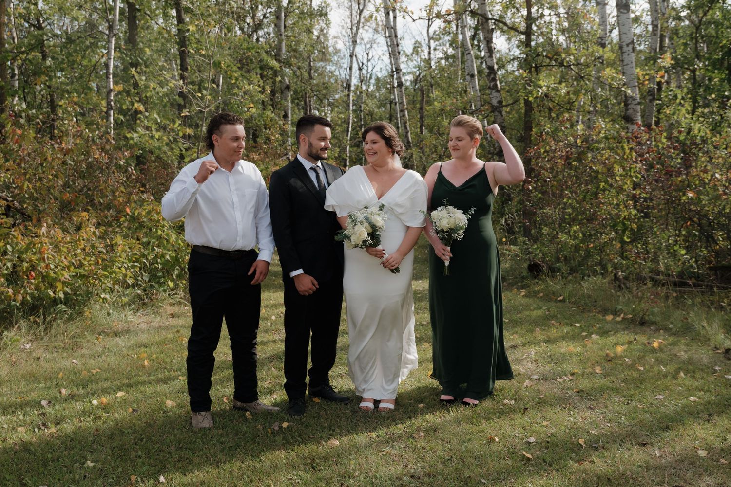 A small wedding party poses together on a grassy area with autumn trees in the background.